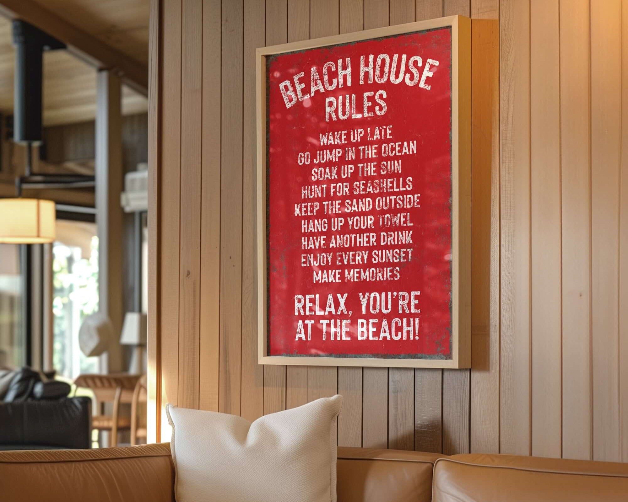 A Beach House Rules Sign in Real Red with rusted edges hangs above a tan couch in a cozy, wood-paneled living room, adding the perfect touch of home wall decor.