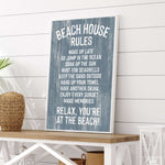 The Beach House Rules Sign, Painted Wood in Harbor Blue, sits on a white table amid coastal decor and plants—a perfect touch for your beach house decor or as eye-catching coastal wall art.