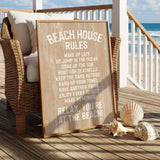 a wooden sign with beach rules, placed on a wooden deck with wicker furniture and seashells nearby, overlooking the ocean.