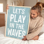a woman holding a sign that says let&#39;s play in the waves