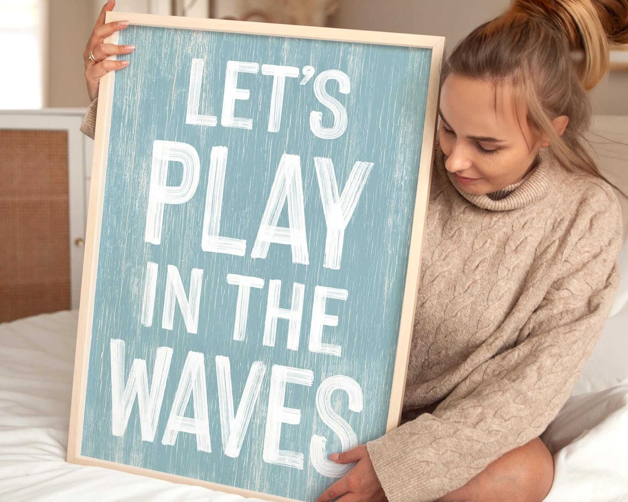 a woman holding a sign that says let's play in the waves