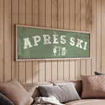 a cozy living room with a wooden wall and a green sign that reads "APRÈS SKI" in white letters. The sign also includes a beer mug and a wine glass, suggesting a festive or celebratory atmosphere.