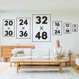 A woman sits on a sofa under the Après Ski Lift Couple Wall Art, Yellow Print, which is displayed in various frame sizes in a modern living room.