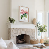 a cozy living room with a stone fireplace, a framed painting of pink flowers hanging above it, and a white sofa. The room is decorated with potted plants and a woven basket, creating a warm and inviting atmosphere.