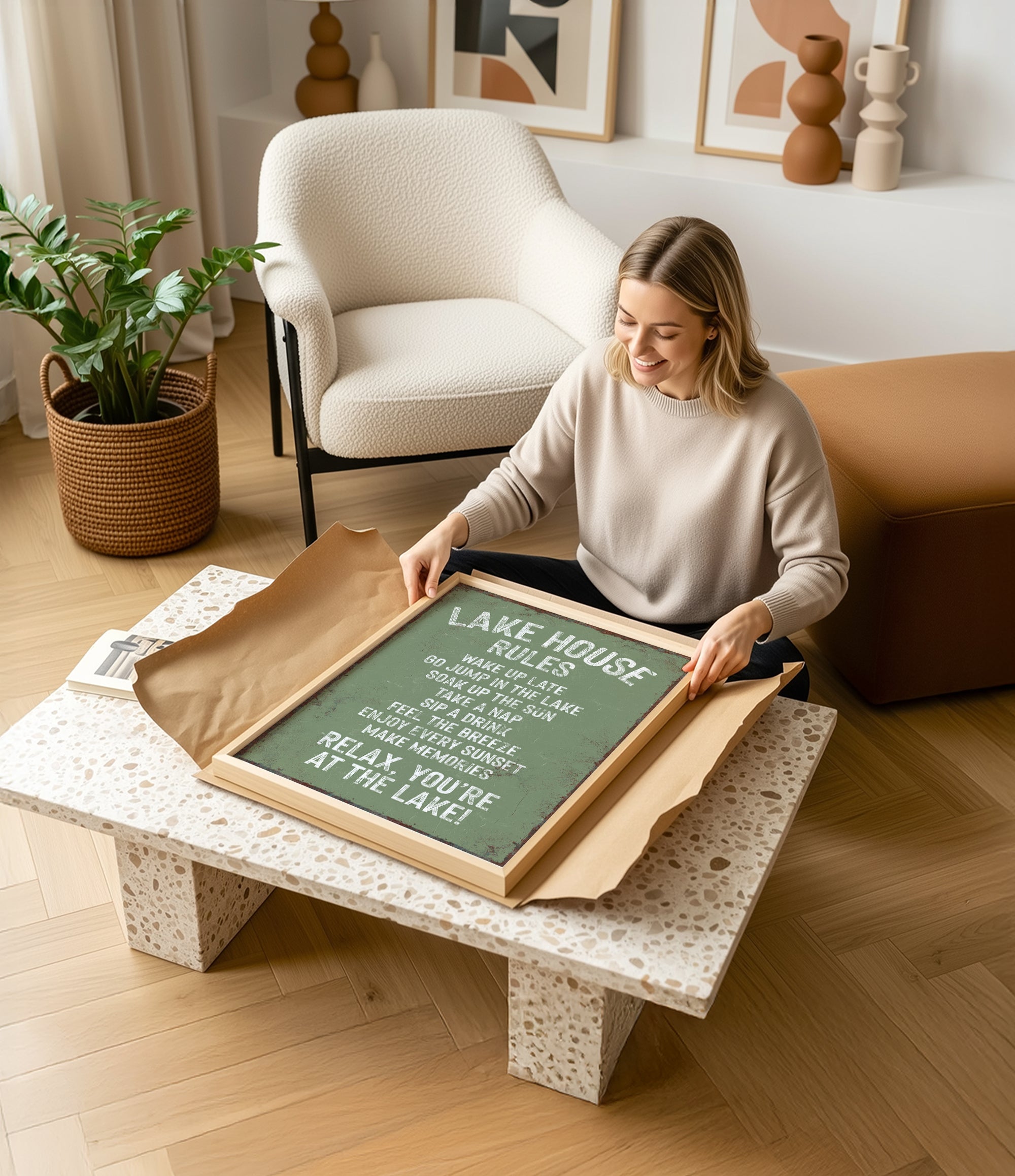 A woman is sitting on the floor in a living room, holding a framed sign with text on it.