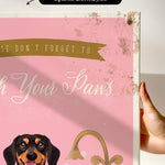 a hand holding a pink canvas print with a dog's face and the text "Don't forget to wash your paws" printed on it.