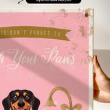 a hand holding a pink canvas print with a dog's face and the text "Don't forget to wash your paws" printed on it.