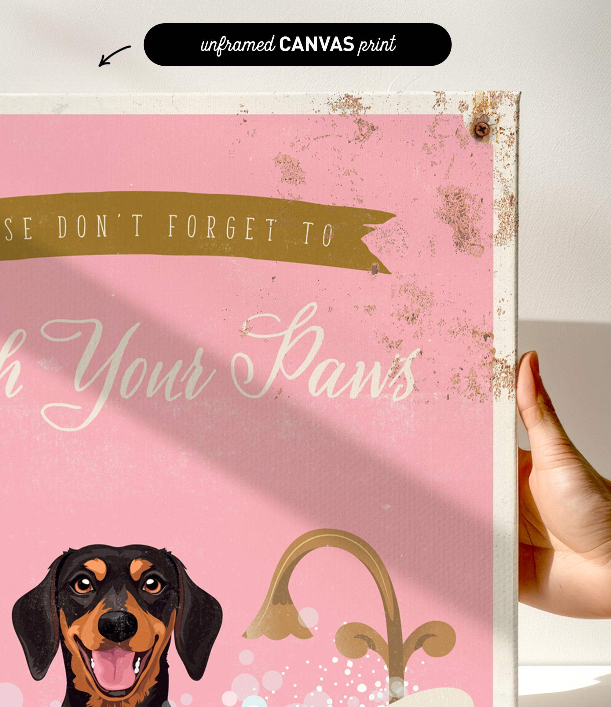 a hand holding a pink canvas print with a dog's face and the text "Don't forget to wash your paws" printed on it.