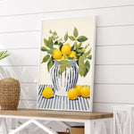 A framed painting of a vase filled with lemons and leaves is displayed on a white wooden table.