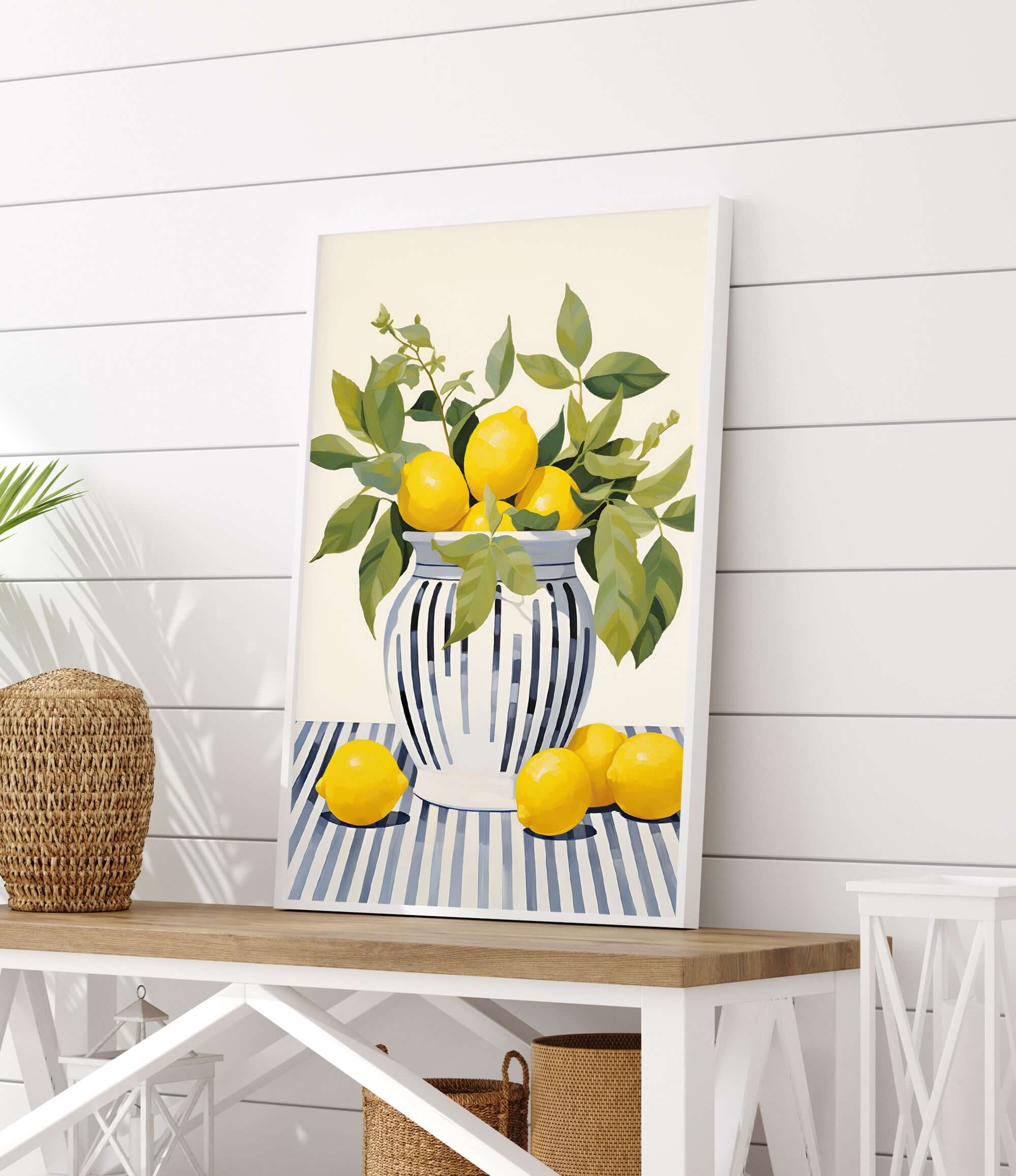 A framed painting of a vase filled with lemons and leaves is displayed on a white wooden table.