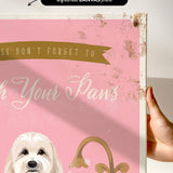 a hand holding a framed canvas print with a pink background and a white dog. The text on the canvas reads "Don't forget to wash your paws".