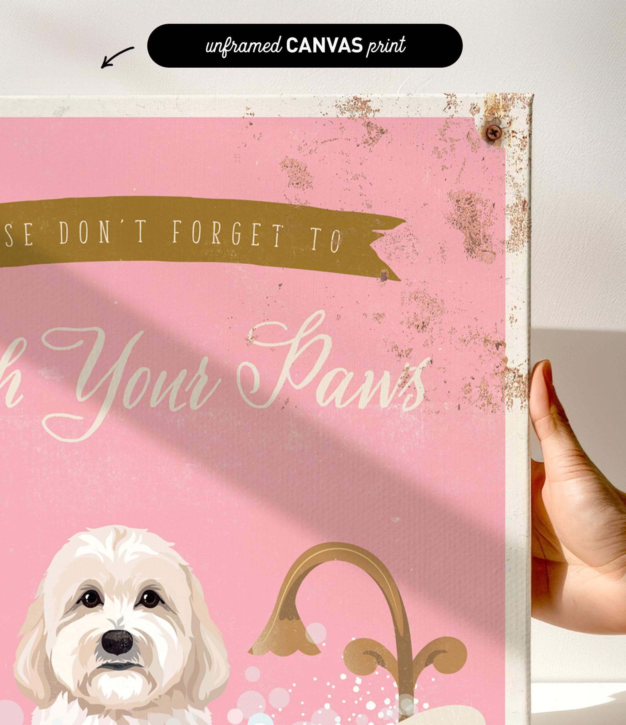 a hand holding a framed canvas print with a pink background and a white dog. The text on the canvas reads "Don't forget to wash your paws".