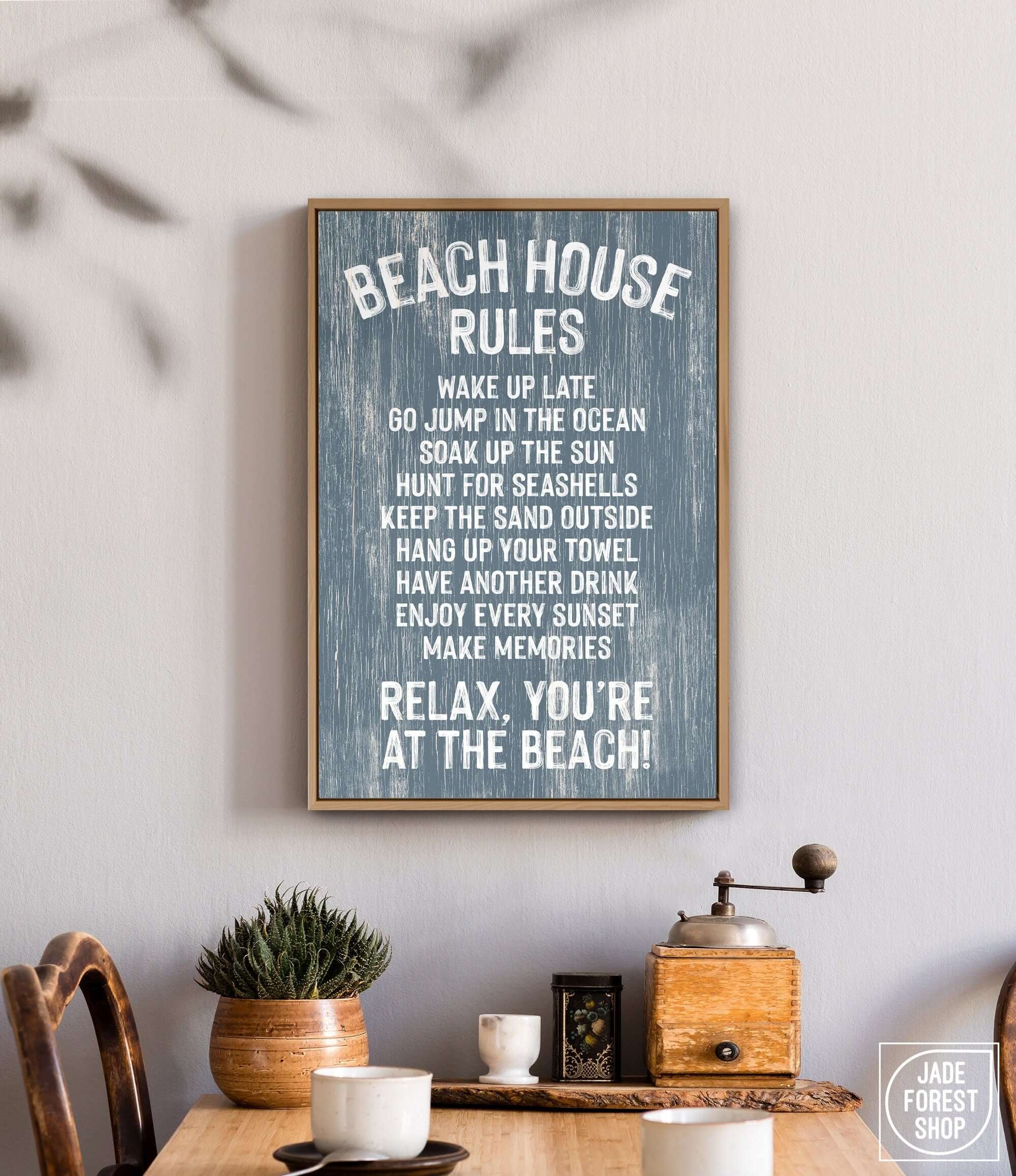The Beach House Rules Sign in painted wood, harbor blue, hangs above a table with plants and a coffee grinder, bringing coastal charm and wall art style to your space.