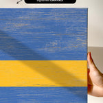a hand holding a piece of wood with a yellow and blue stripe