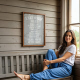 A woman sits on a bench in front of a sign that reads "LAKESHOUSE RULES" in a wooden cabin setting.