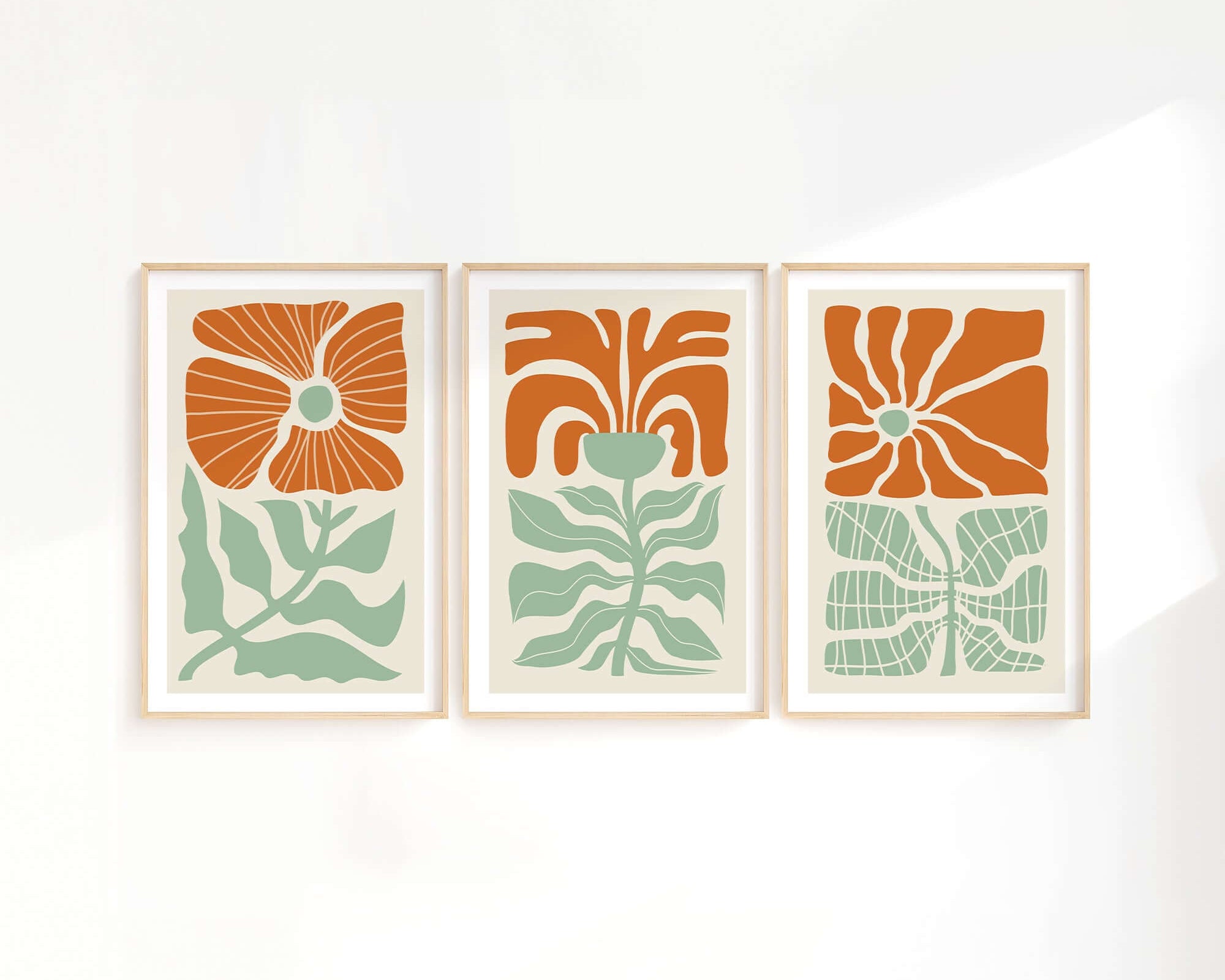 The Flower Blocks Triptych | Set of Three Prints | 012 features abstract floral designs in orange and green, framed and hung on a white wall with soft light—ideal for enhancing your home decor.