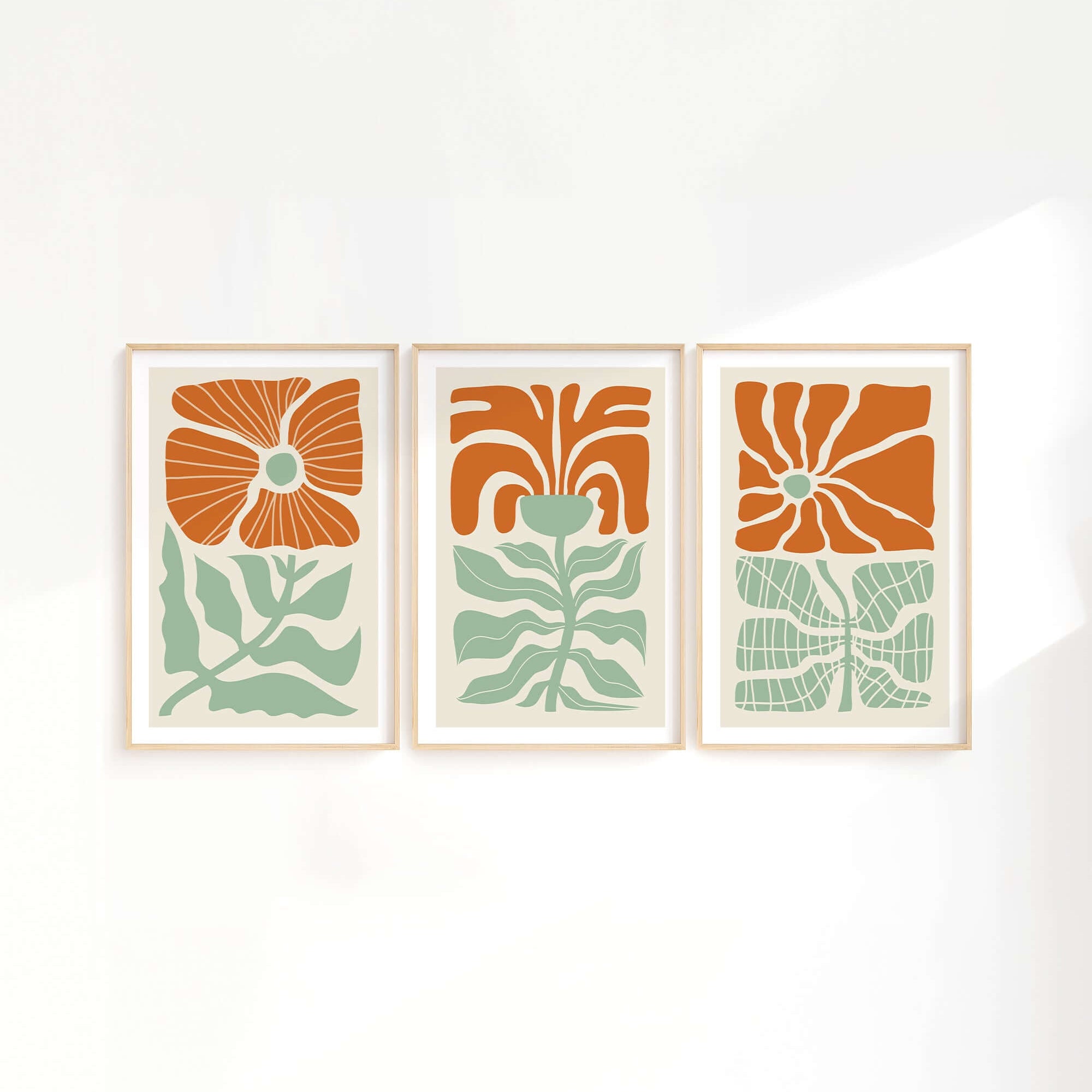 The Flower Blocks Triptych | Set of Three Prints | 012 features abstract floral designs in orange and green, framed and hung on a white wall with soft light—ideal for enhancing your home decor.