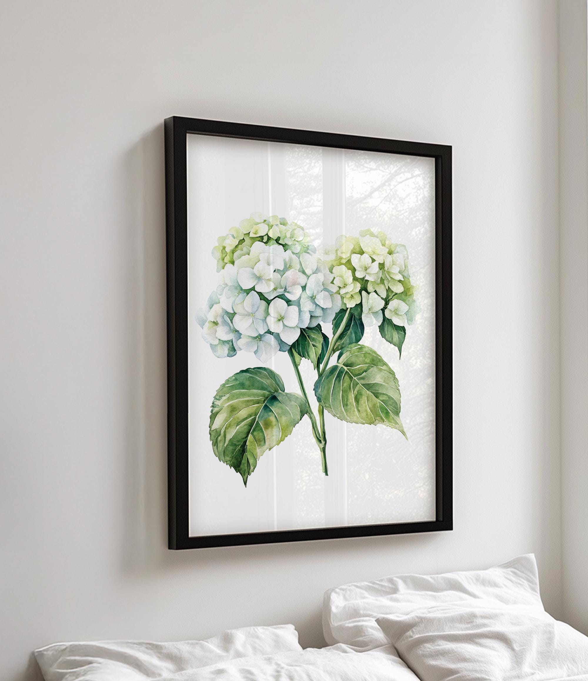 a framed watercolor painting of two white hydrangea flowers with green leaves, hanging on a wall above a bed with white pillows.