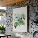 a large framed painting of white hydrangea flowers hanging on a stone wall.