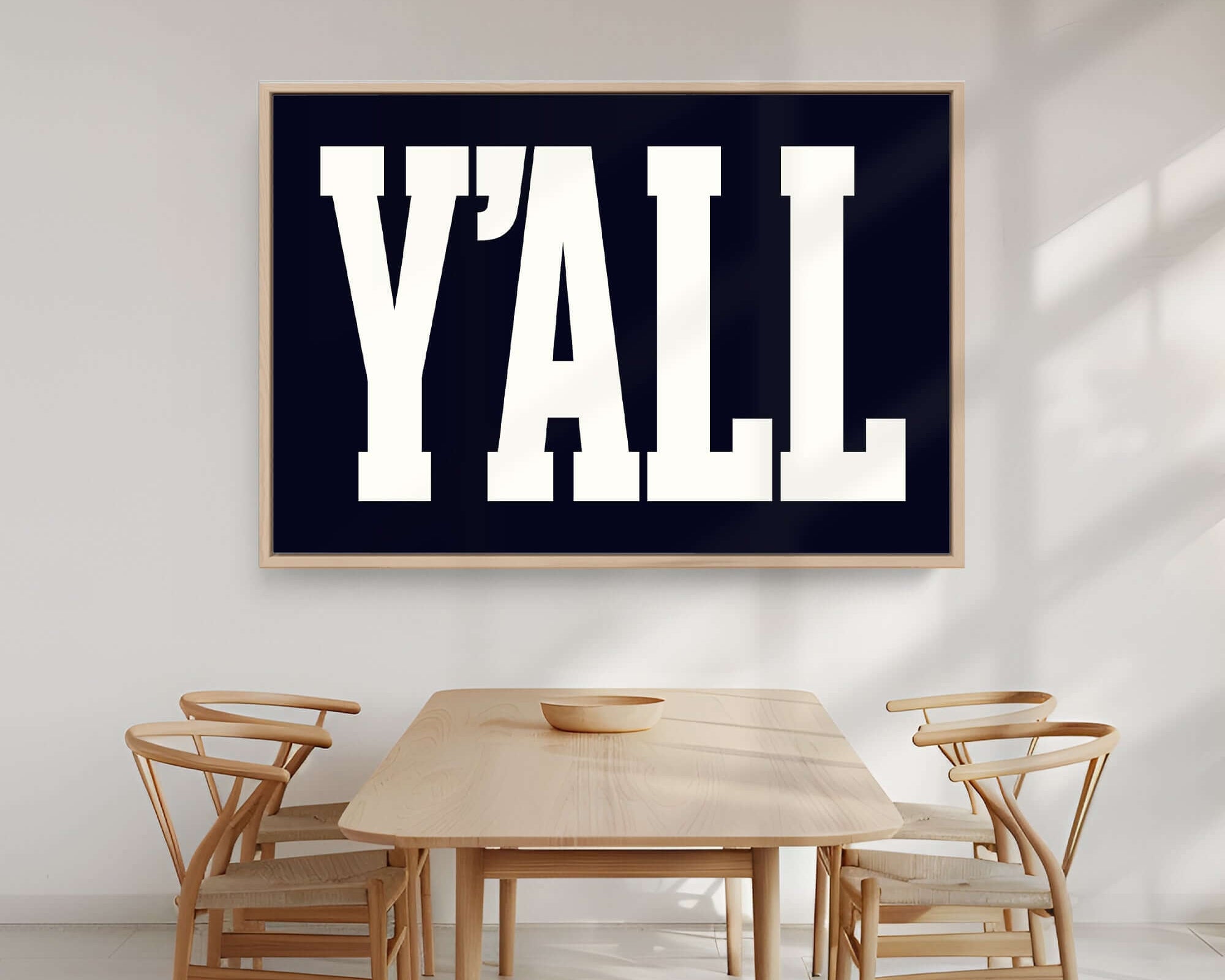 A dining area featuring four wooden chairs, a table, and the black "Y'all Sign Print" on the wall brings modern farmhouse charm to your home decor.