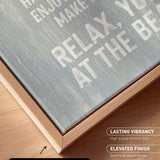 a close-up view of a wooden frame with a canvas print on it. The text on the canvas print reads "HAPPY HAVE A MEAN MAKE ENJOY THE RELAX. YO BE". The text is in white and is located on the canvas print itself.