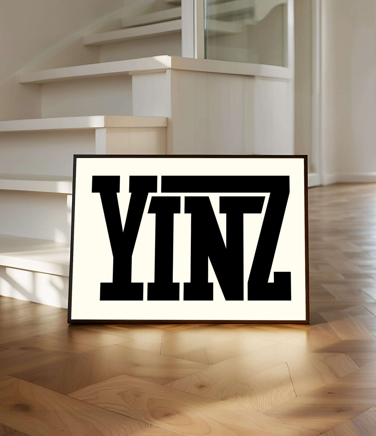 The Yinz Sign Print in off white features bold black letters, framed and displayed on a wooden floor by white stairs, bringing modern farmhouse charm to your home decor.