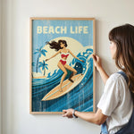 A woman is hanging a framed poster of a woman surfing on a wall.