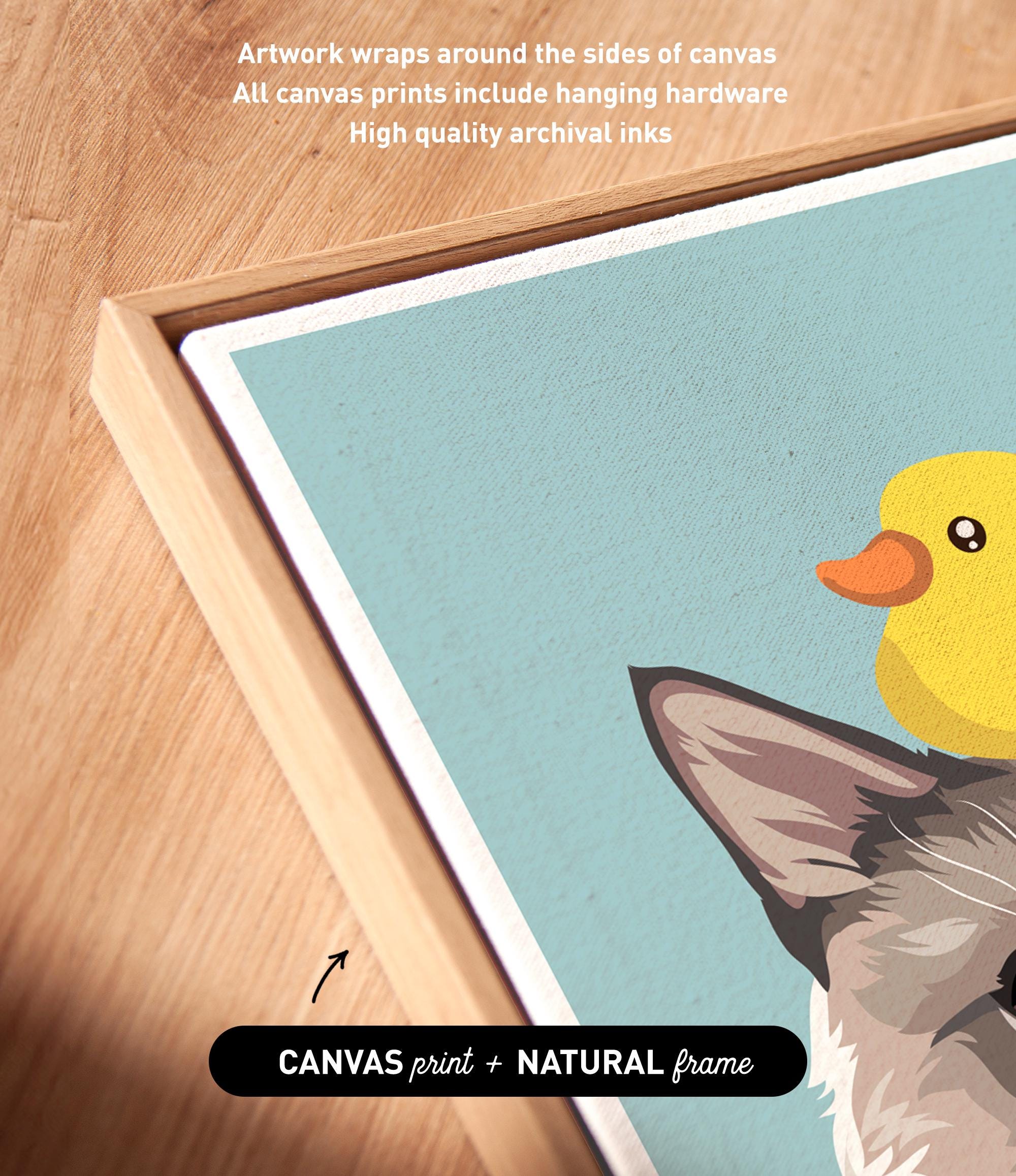 a close-up view of a framed artwork depicting a cat and a yellow duck. The artwork is framed in a natural frame, and the text indicates that the artwork wraps around the sides of the canvas, and all canvas prints include hanging hardware and high-quality archival inks.
