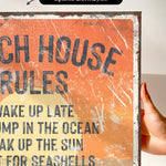 The image is a close-up of a textured, orange-colored sign with the text "ACH HOUSE RULES" written on it.