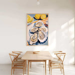 a dining room with a wooden table and four chairs. Above the table, there is a large painting of oysters and lemons on a white wall.