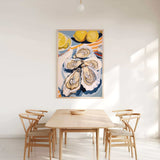 a dining room with a wooden table and four chairs. Above the table, there is a large painting of oysters and lemons on a white wall.