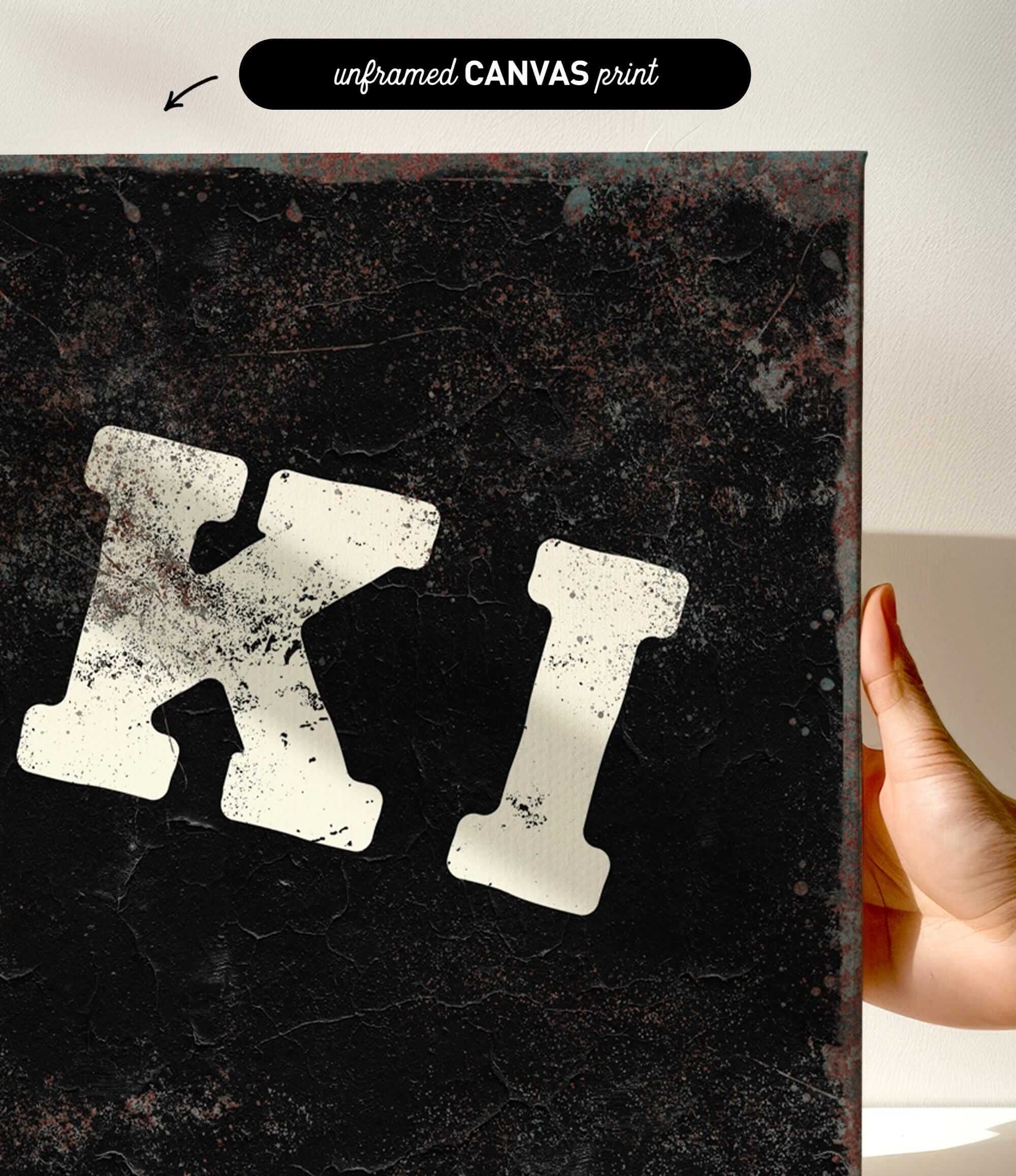 a hand holding a canvas print with a large, distressed letter "K" on it.