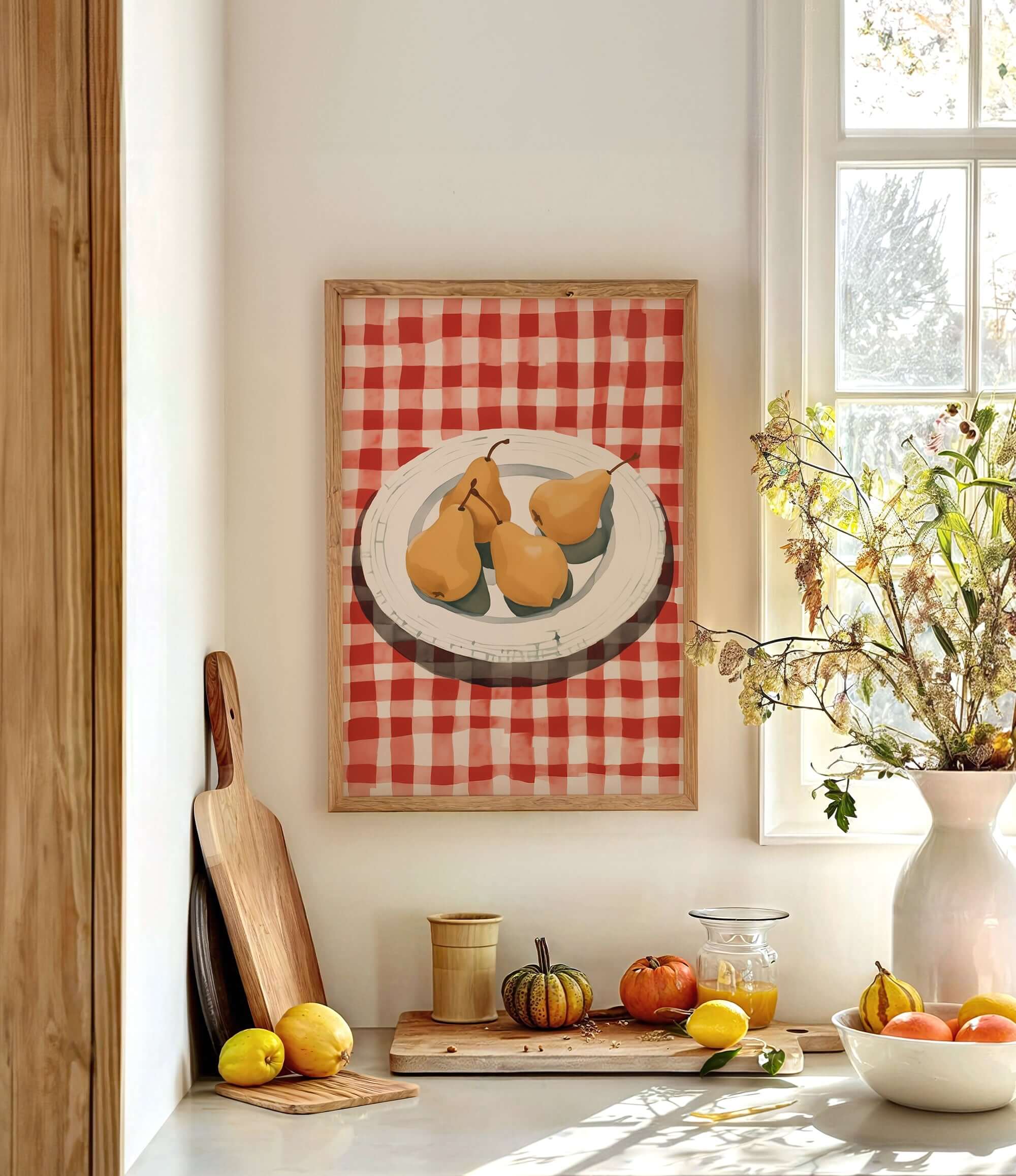 a kitchen counter with a framed painting of pears on a red and white checkered tablecloth, a wooden cutting board, a vase of flowers, and various fruits and vegetables on the counter.