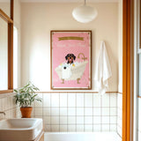 A bathroom with a pink bathtub, a towel, and a plant. Above the bathtub is a framed poster with a dog and the text "Please wash your paws".