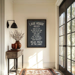 a hallway with a framed sign that reads "LAKESHORE RULES" hanging on the wall. The hallway has a wooden table, a lamp, and a rug on the floor. There is also a window with a view of trees outside.