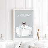 A framed poster with a cat sitting in a bathtub filled with bubbles, accompanied by the text "WASH YOUR PAWS" on a white wall.