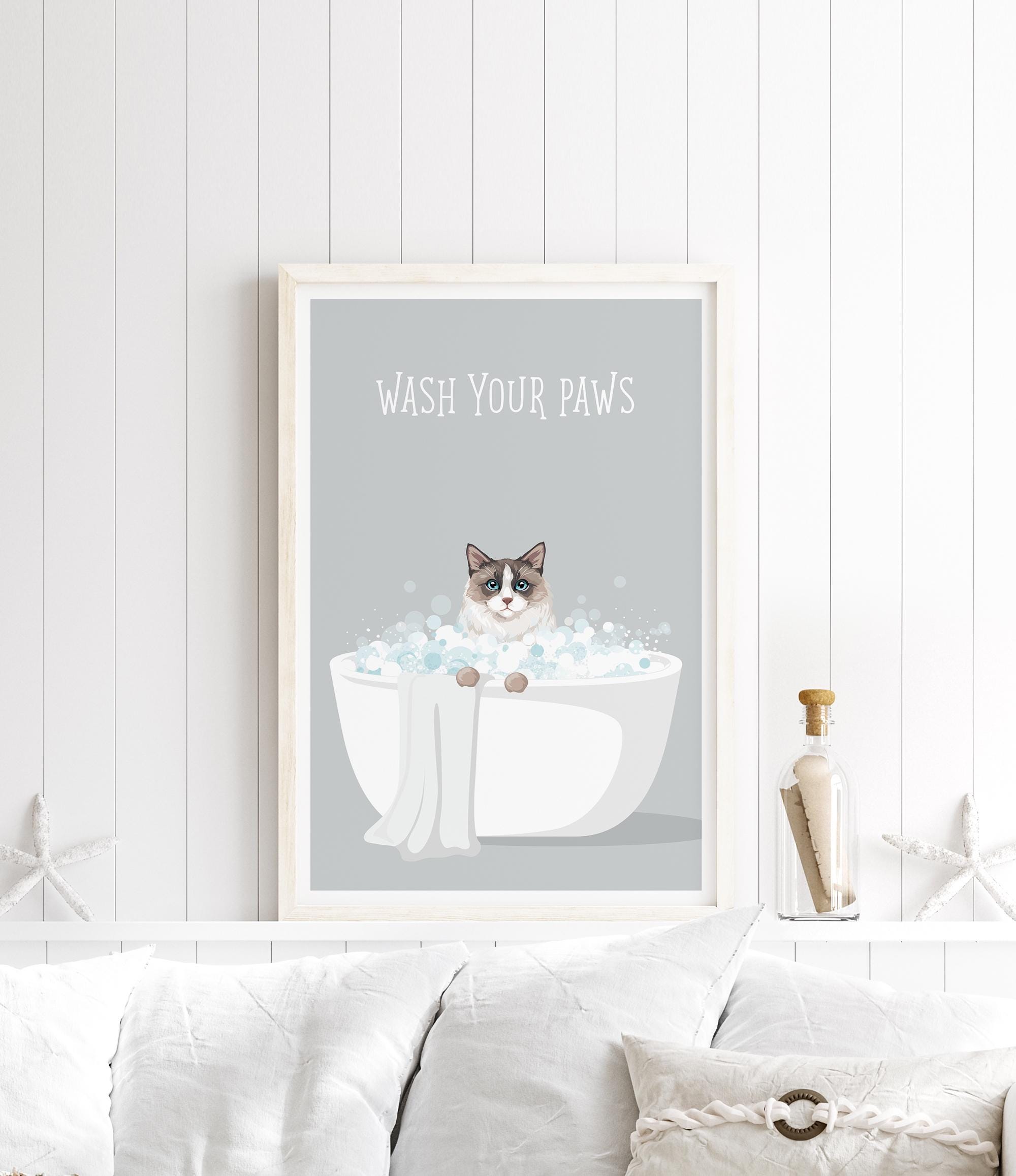 A framed poster with a cat sitting in a bathtub filled with bubbles, accompanied by the text "WASH YOUR PAWS" on a white wall.