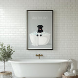 A framed poster with a black dog sitting in a bathtub, surrounded by bubbles, is displayed on a white tiled wall above a white freestanding bathtub.