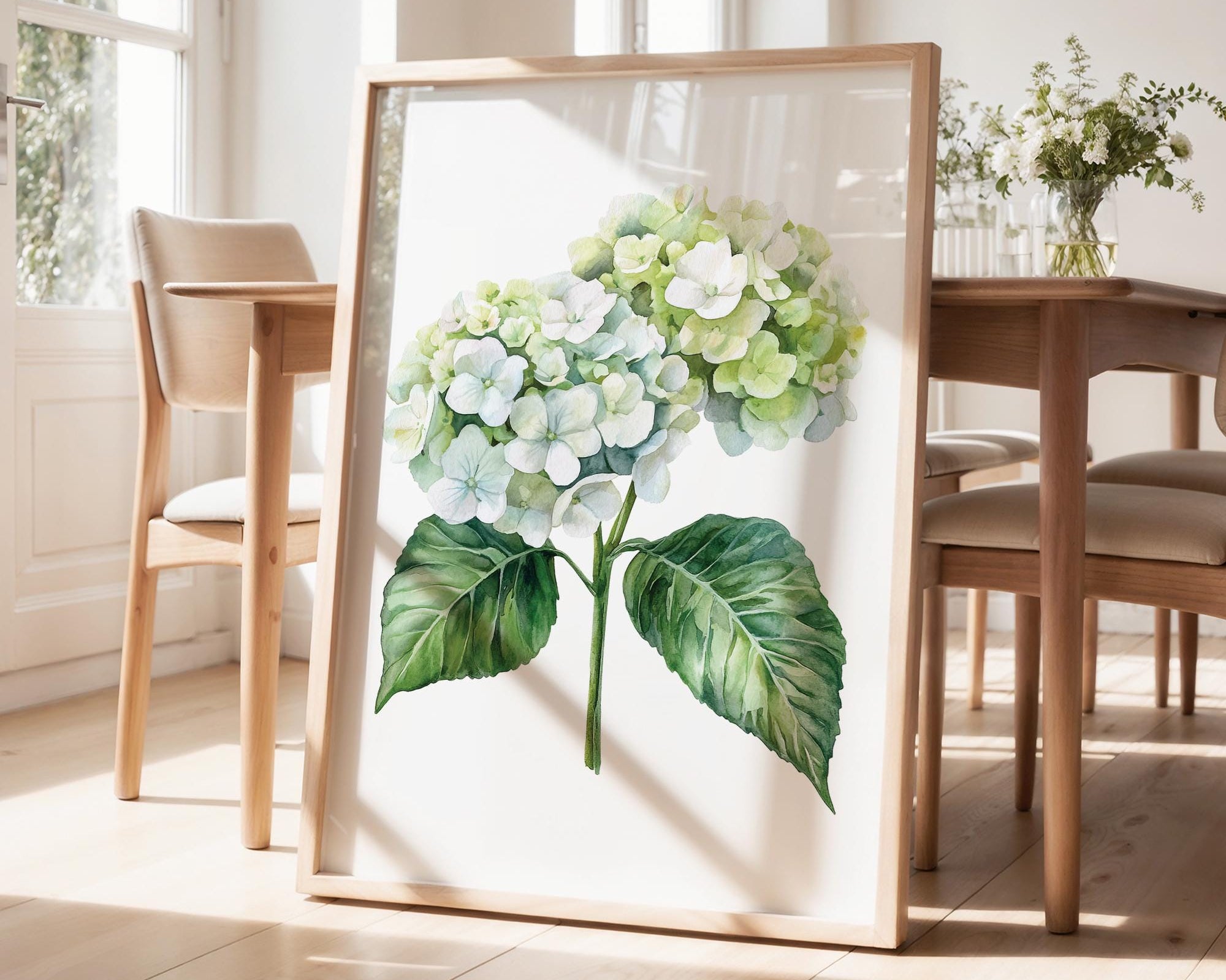 a framed watercolor painting of a hydrangea flower on a wooden table, with a vase of flowers and a pendant light in the background.