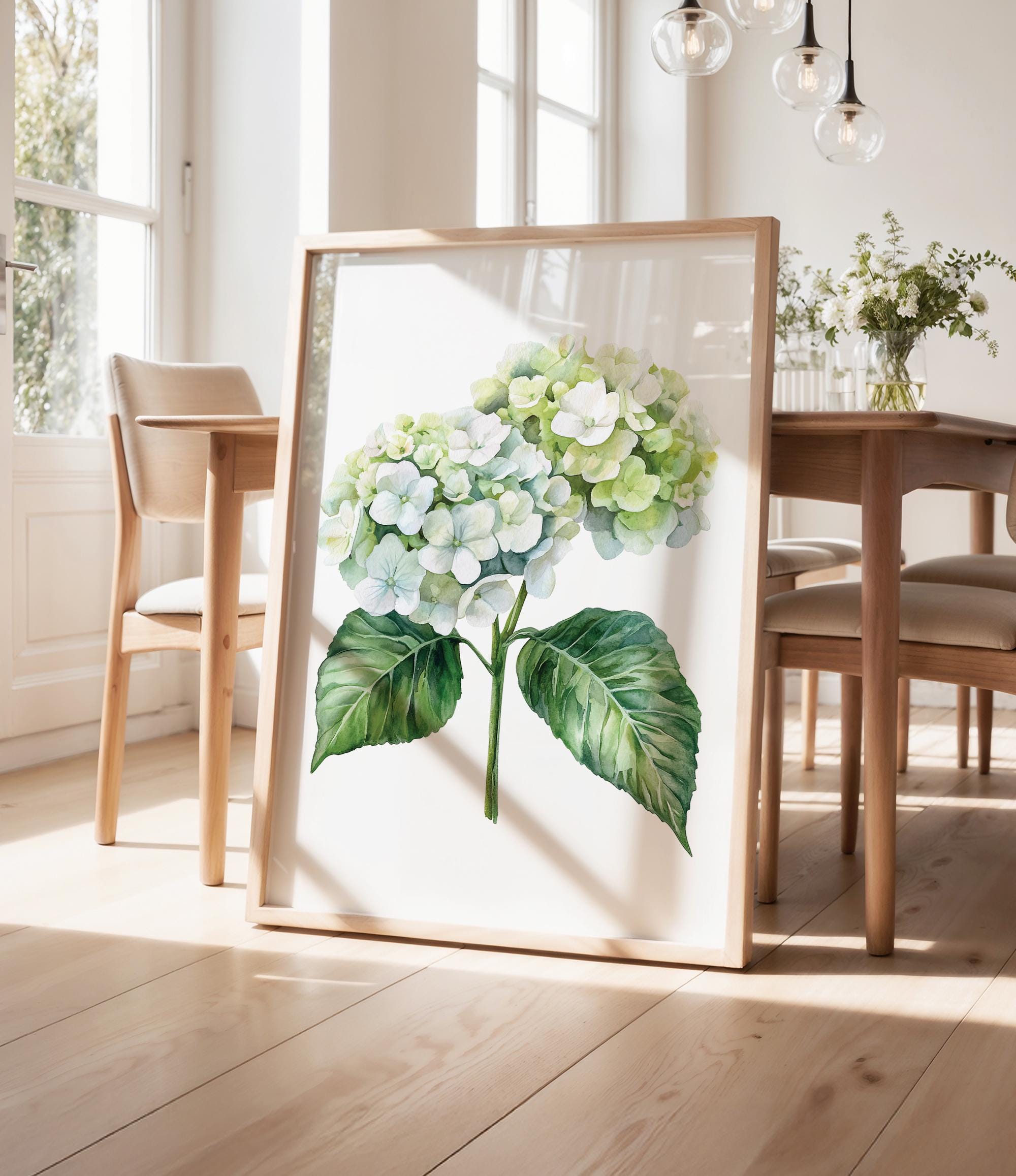 a framed watercolor painting of a hydrangea flower on a wooden table, with a vase of flowers and a pendant light in the background.