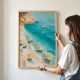 A woman is hanging a framed painting of a beach scene on a wall.