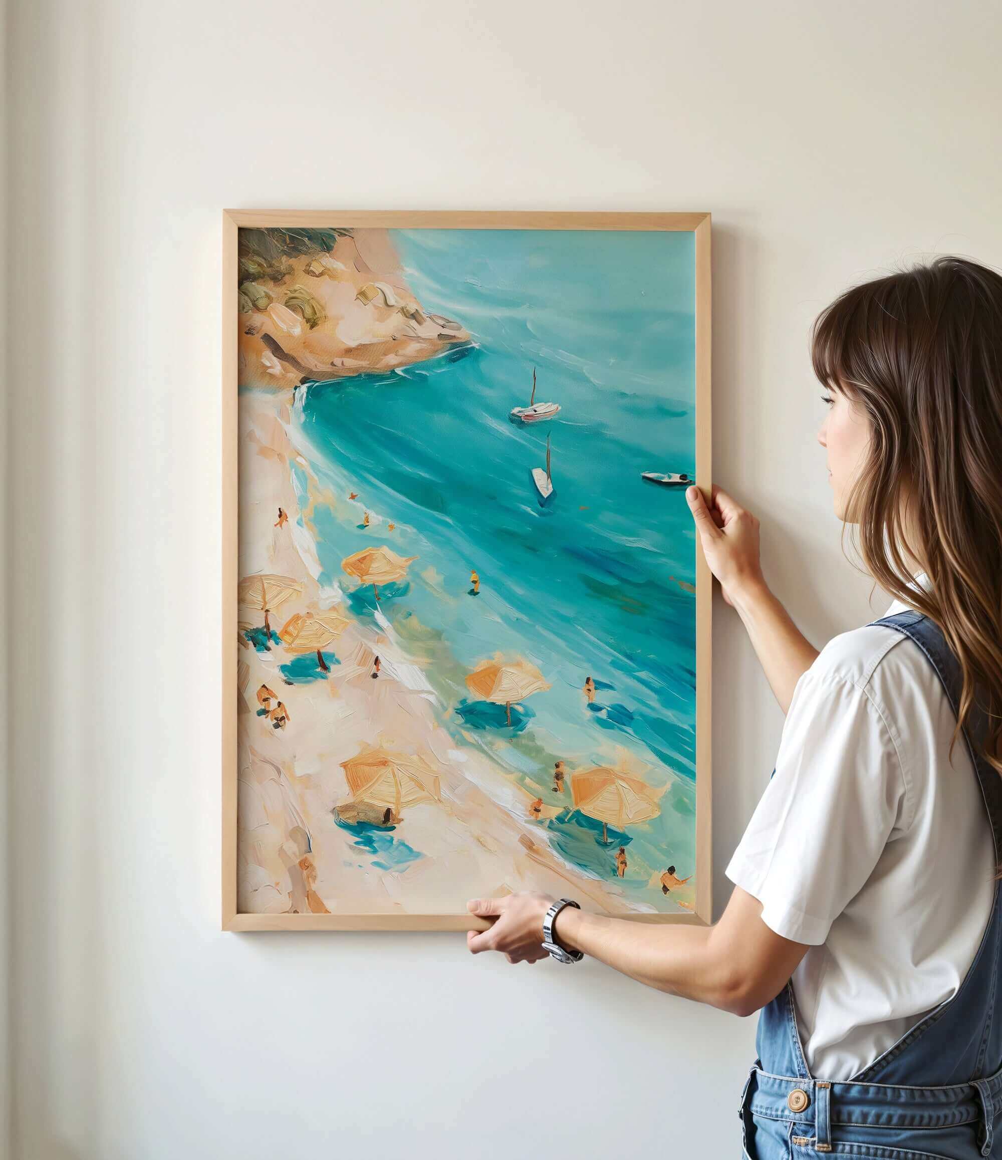 A woman is hanging a framed painting of a beach scene on a wall.