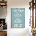 a sign that reads "LAKESHOUSE RULES" hanging on a wall in a room with a fireplace and a vase.