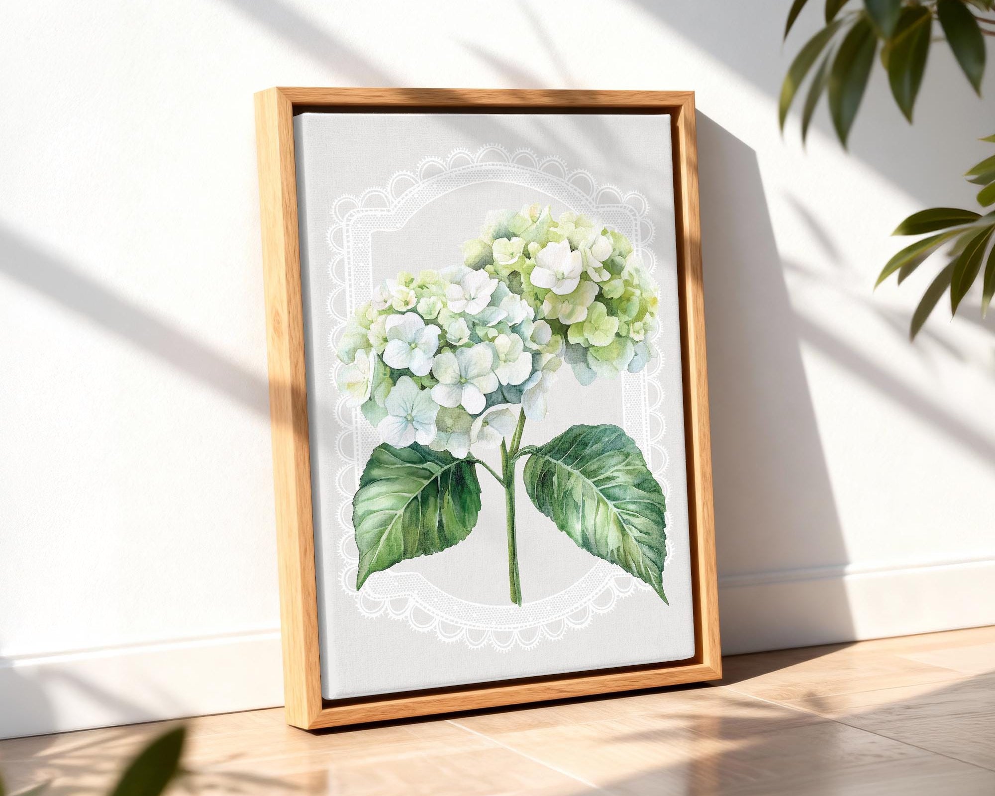 A framed watercolor painting of a white hydrangea flower is displayed on a wooden floor, with a plant visible in the background.