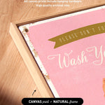 The image is a close-up of a pink canvas with the text "Please don't forget to wash your hands" written on it. The canvas is framed in a natural frame, and there is a small arrow pointing to the bottom right corner of the canvas.