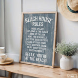 The Beach House Rules Sign, Painted Wood, Harbor Blue, sits on a wooden table beside a plant and straw hat—perfect coastal decor for adding charm to any space.