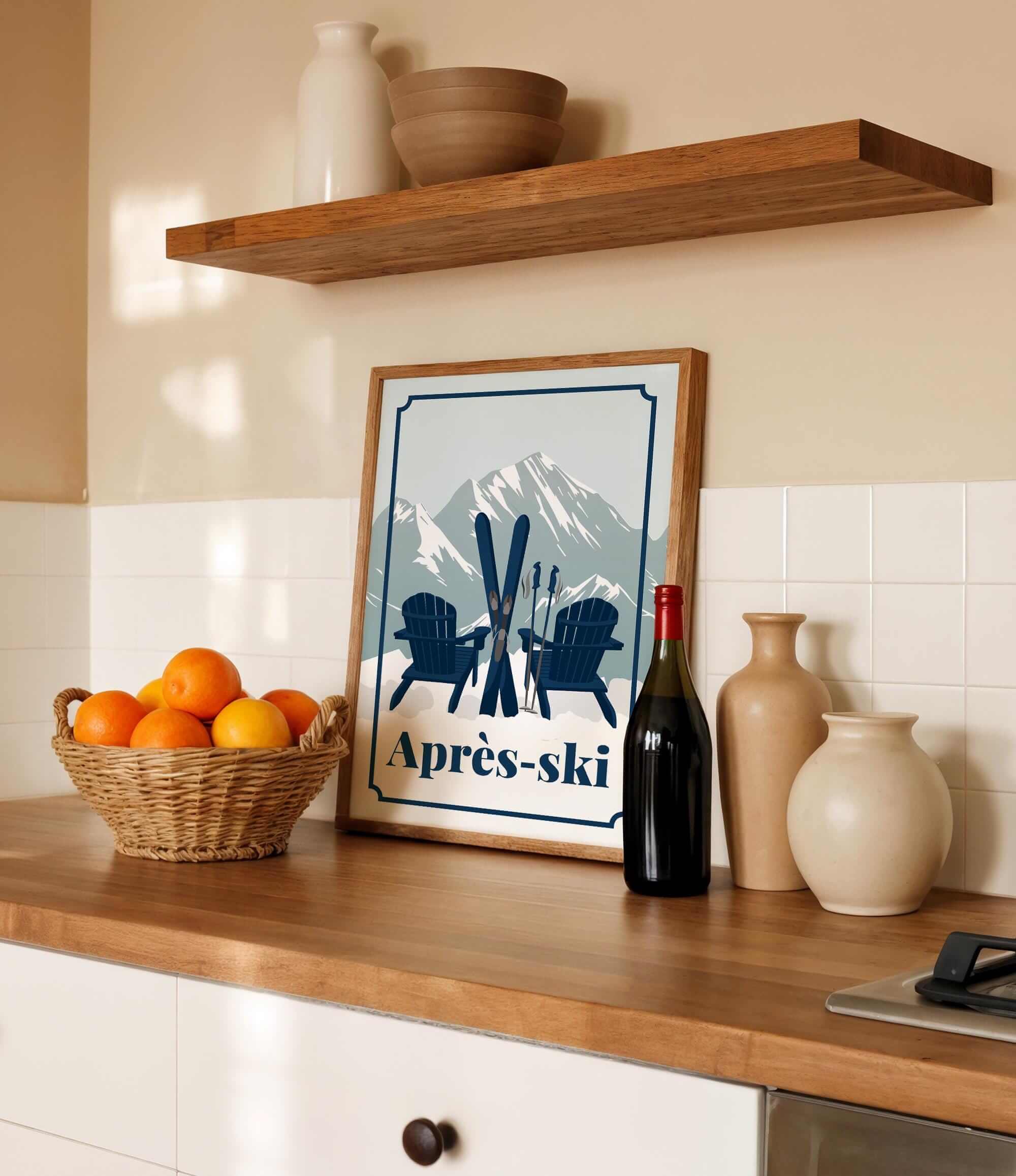 a kitchen counter with a framed poster of a mountain landscape with skis and Adirondack chairs,, a basket of oranges, a bottle of wine, and various decorative items such as vases and a bowl.