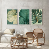 a modern living room with a wicker chair, a coffee table, and three framed botanical leaf art prints on the wall.