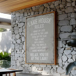 a framed sign with a list of rules for a lake house, mounted on a stone wall.
