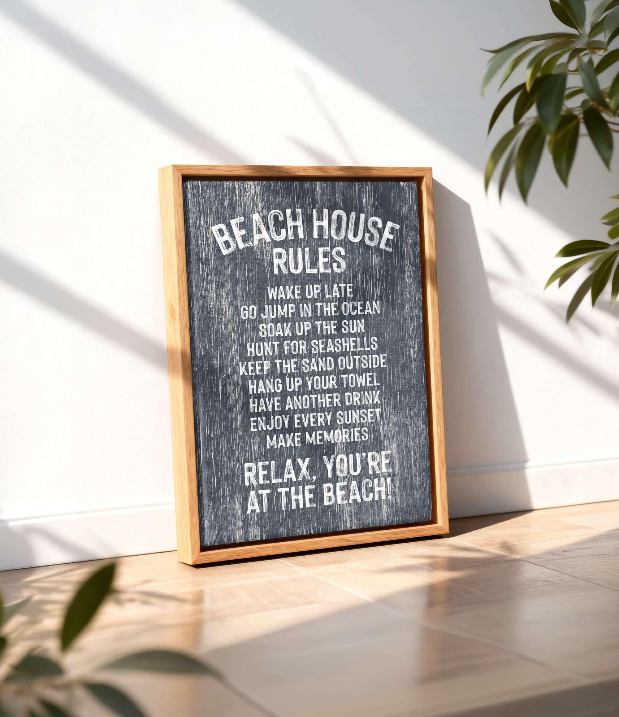 A framed sign with the text "BEACH HOUSE RULES" displayed on a wooden surface, with a plant in the background.